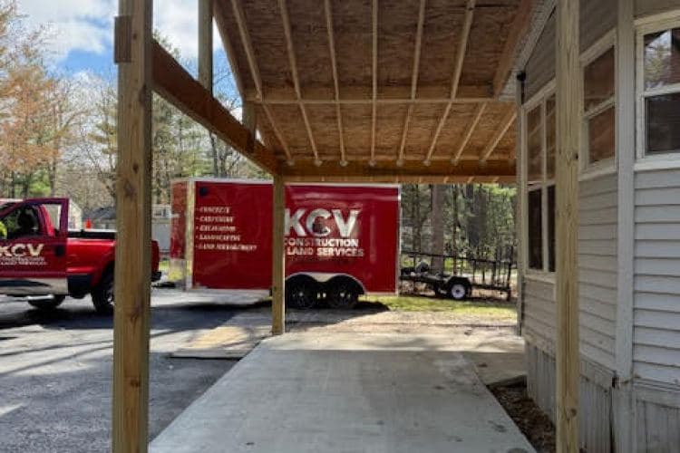 KCV Construction truck and trailer by a newly constructed porch in a wooded area.