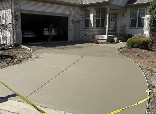 Newly poured concrete driveway at a residential home, with caution tape visible.