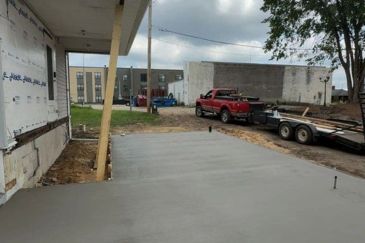 Freshly poured concrete slab for a construction project beside a building and parked vehicles.
