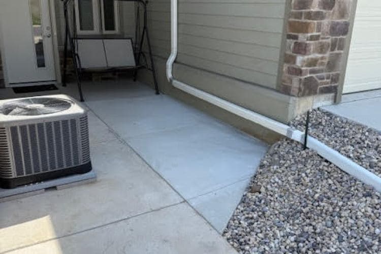 Air conditioning unit beside a porch with concrete pathway and gravel landscaping.