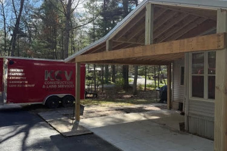 KCV Construction trailer beside newly built carport in a wooded area.