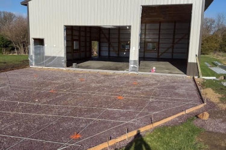 Newly laid concrete foundation with reinforcing mesh for a metal building construction site.