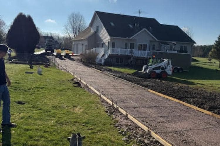 Construction of a gravel driveway next to a house, featuring landscaping and machinery.
