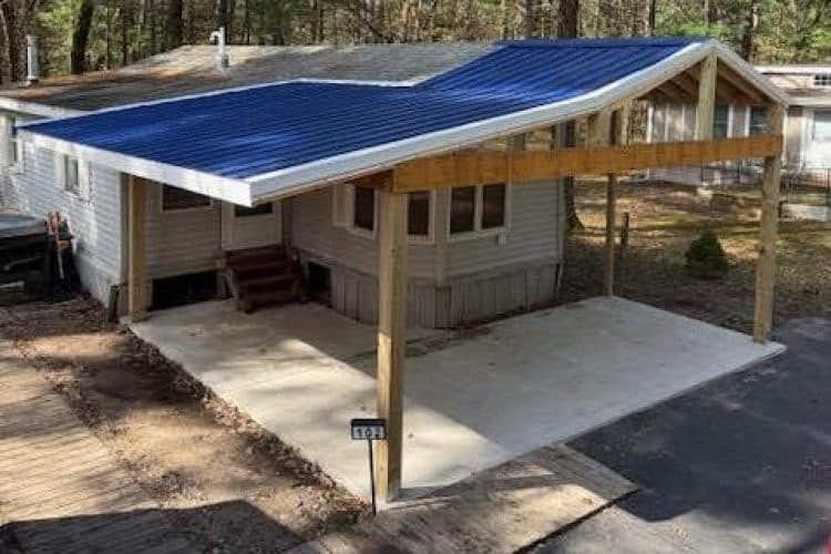 Modern home with a blue metal roof and spacious carport in a wooded area.