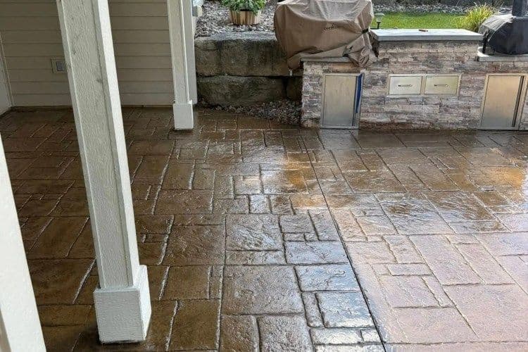 Decorative stamped concrete patio with a stone wall and dry landscaping.