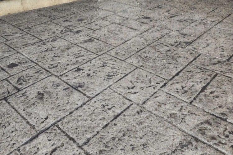 Textured concrete surface with a stamped stone pattern and visible aging signs.