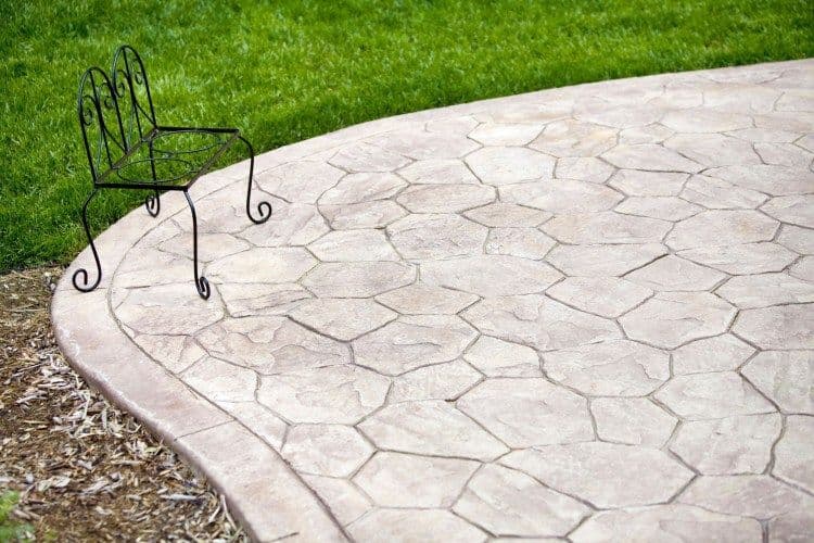 Decorative concrete patio with a metal chair and lush green grass in the background.