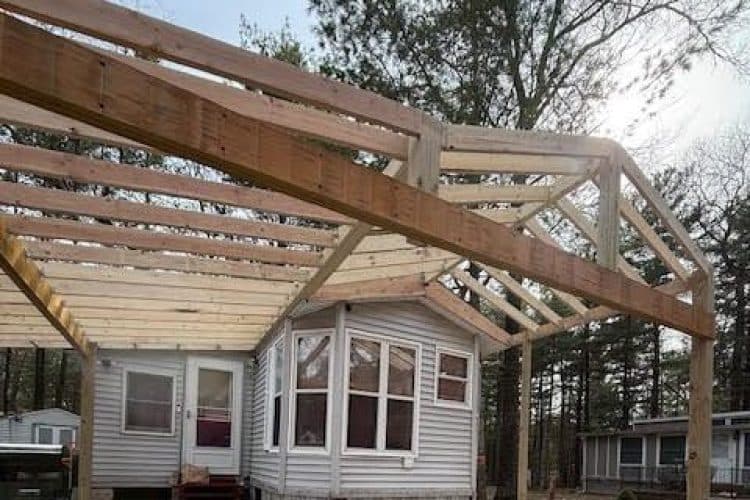 House under construction with wooden framework and exposed beams in a forested area.