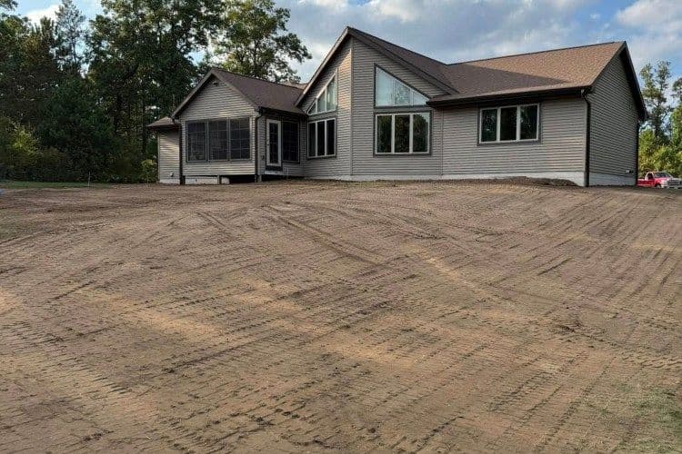 Newly built modern house with large windows and a cleared landscape.