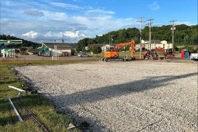 Construction site with excavators and gravel parking lot under a blue sky.