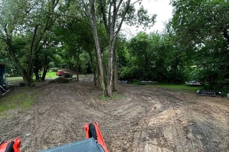 Cleared area with trees, muddy ground, and equipment in a rural setting.