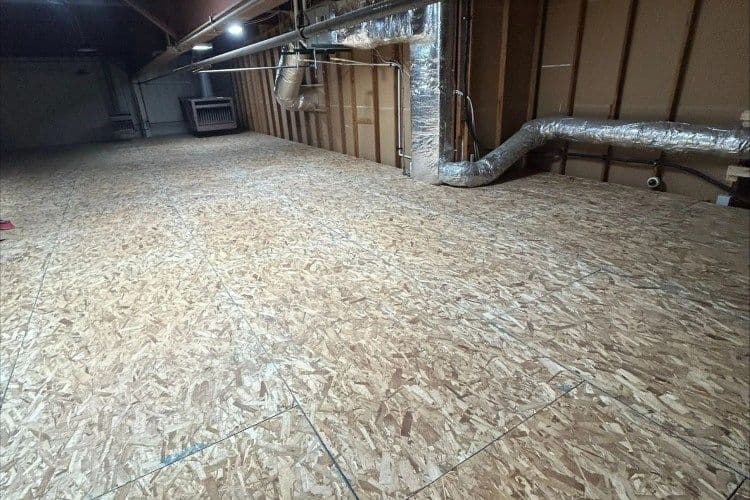 Spacious unfinished basement with plywood flooring and exposed ductwork.