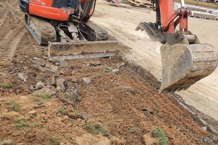 Excavator digging and removing dirt on construction site with rocky terrain.