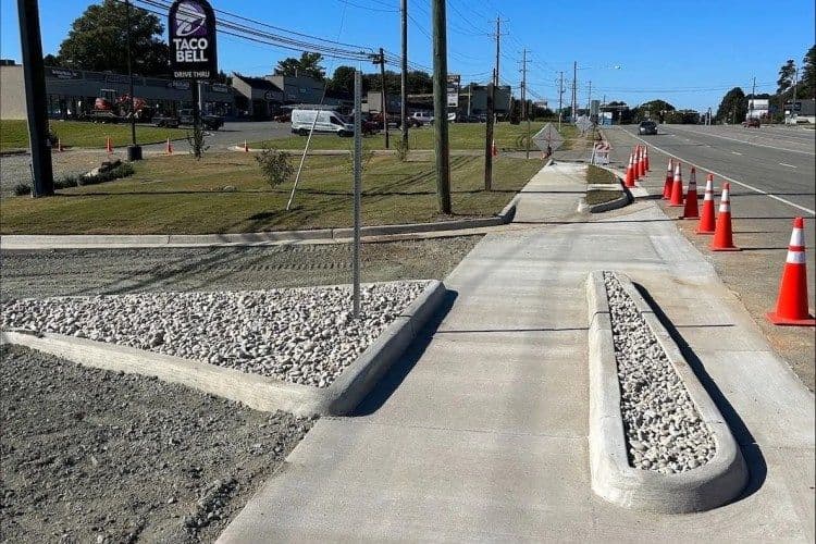 Newly constructed sidewalk with gravel landscaping near Taco Bell and traffic cones.