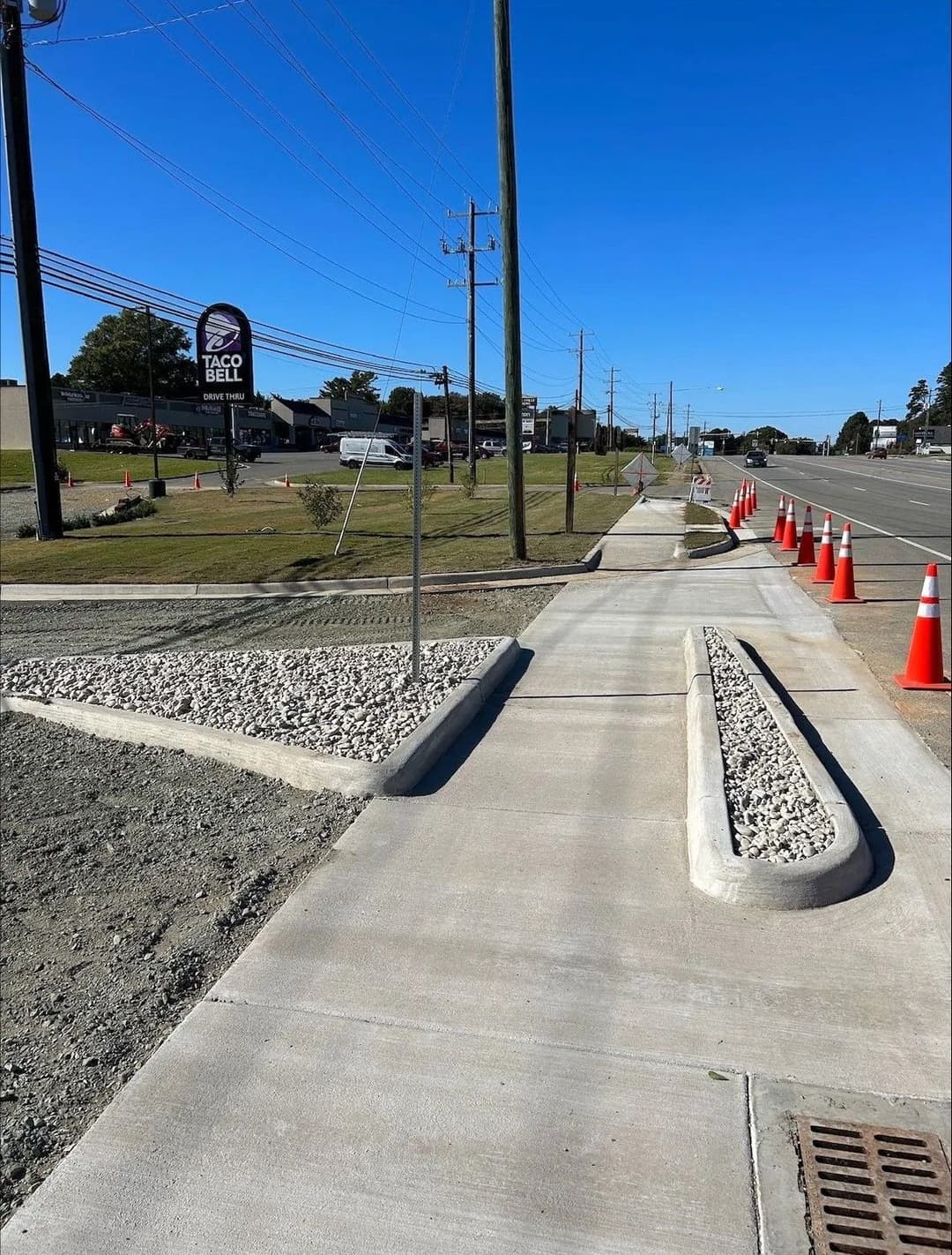 Sidewalk construction with traffic cones, curb, and Taco Bell sign in the background.