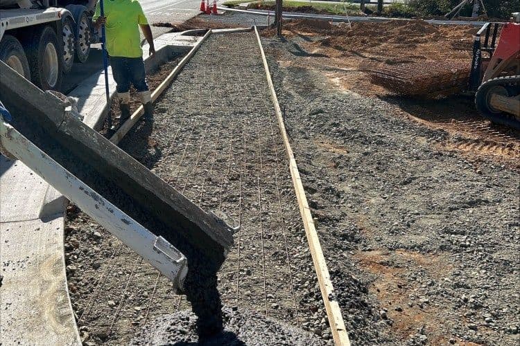 Worker pouring concrete for a construction project, reinforcing mesh visible on site.