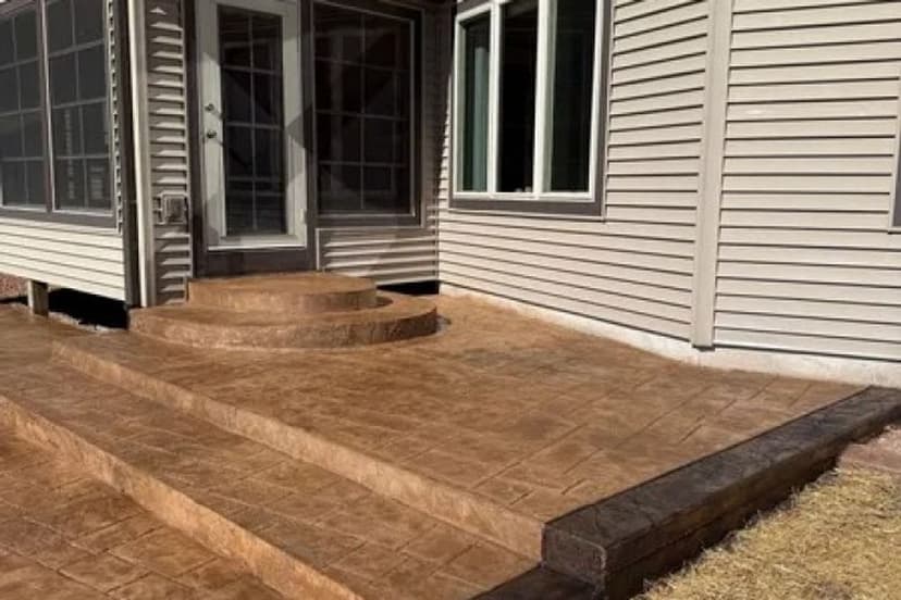 Stamped concrete patio steps leading to a house entrance with large windows.