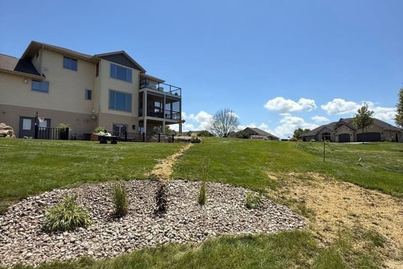 Modern house with deck on green lawn, stone landscaping, and clear blue sky.