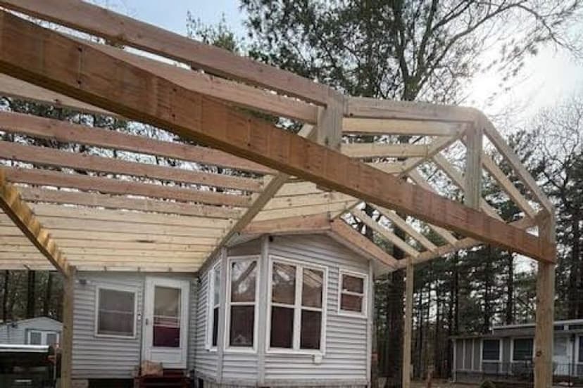 Framing of a wooden structure under construction near a house in a wooded area.