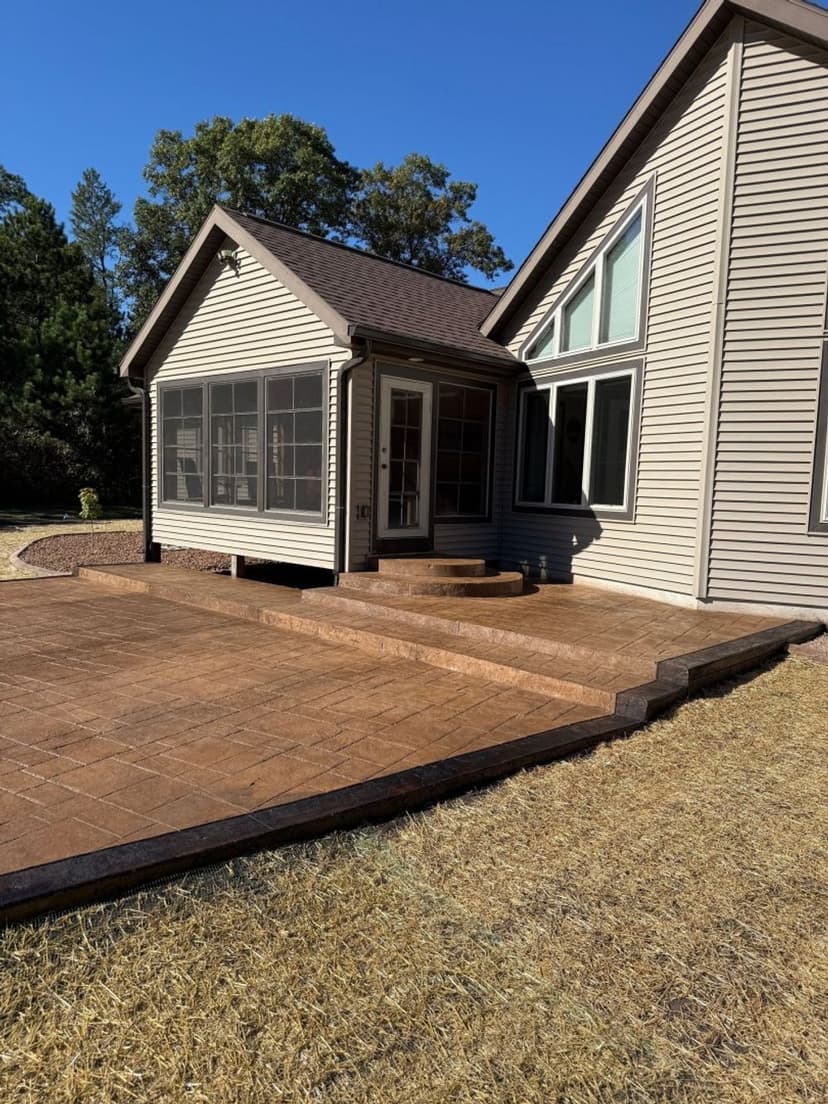 Exterior view of a modern house with a screened porch and stone patio, surrounded by trees.