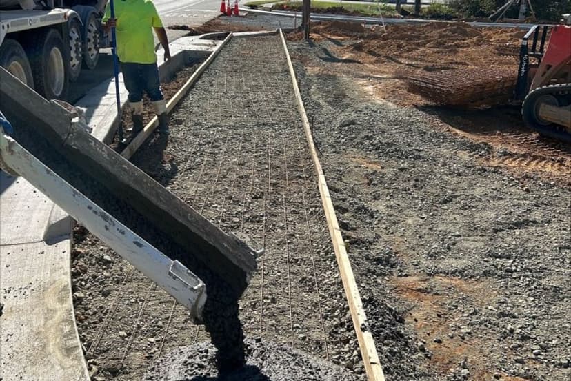 Worker pouring concrete for a sidewalk construction project on a sunny day.