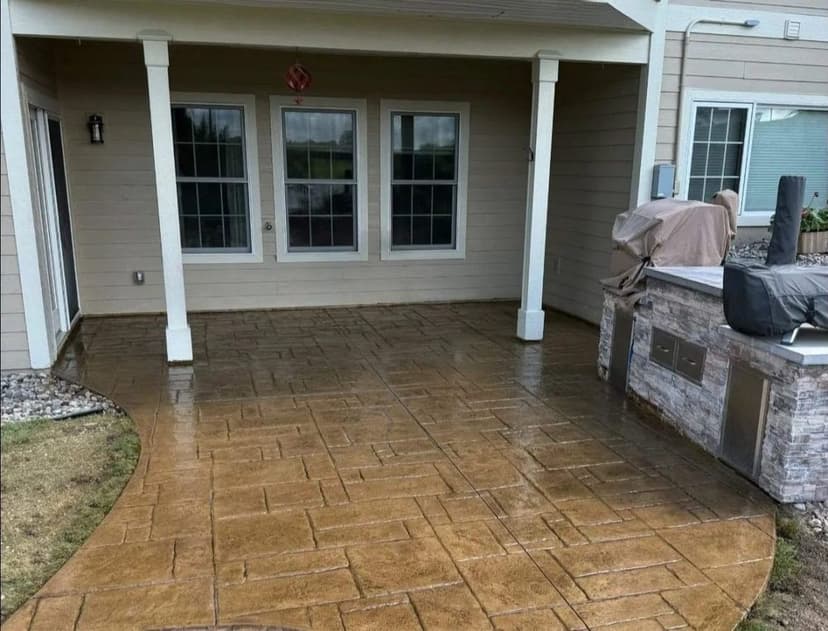 Decorative stamped concrete patio with outdoor grill near a covered porch area.